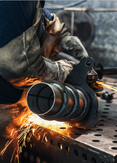 Ein Handwerker schneidet ein Metallrohr mit einem Winkelschleifer. Funken fliegen auf einem perforierten Tisch.